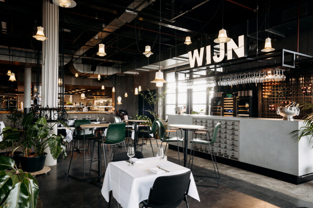 Modern restaurantinterieur aan het John M. Keynesplein met open keuken, wijntafel en industriële details.